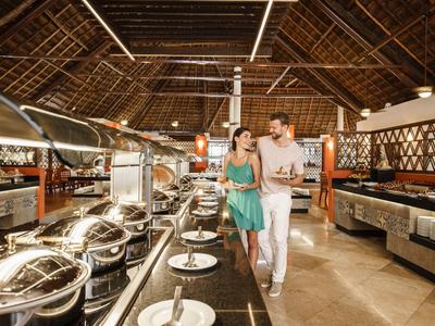 Jeune couple marchant dans un restaurant buffet avec toit de chaume dans une station de vacances.
