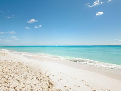 Plage de sable blanc avec eau turquoise claire sous un ciel bleu.