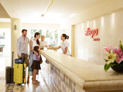 Famille s'enregistrant à la réception d'un hôtel avec une valise jaune.