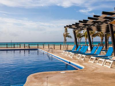 Ein ruhiger Poolbereich mit blauen Liegestühlen und Blick auf den Strand und das Meer.