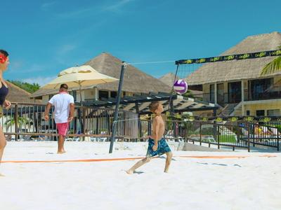 Kinder spielen Volleyball am Strand vor einem Resort bei sonnigem Wetter.