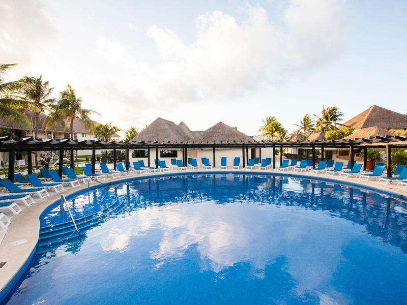 Piscine ronde avec surface d'eau bleue, entourée de chaises longues et de palmiers.