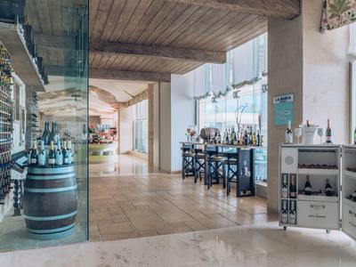 Área luminosa de bodega con vigas de madera, barriles y mesas altas en un hotel.