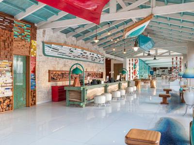 Recepción amplia y luminosa con mostrador largo, sillas blancas y decoración playera en techo y paredes.