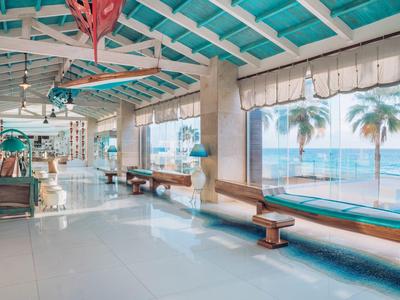 Vestíbulo de hotel luminoso con grandes ventanales y vista a palmeras y mar