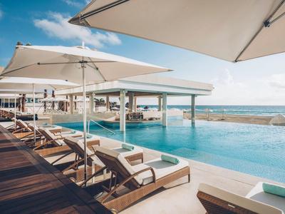 Luxuriöser Poolbereich mit Liegestühlen, Sonnenschirmen, Holzdeck und Meerblick unter blauem Himmel.