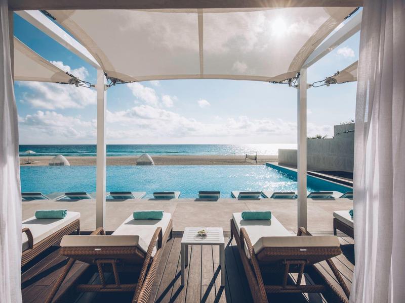 Área moderna de piscina con tumbonas y vista al mar bajo cielo despejado en hotel de playa.