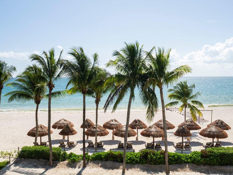 Strand mit Palmen, Strohhüten, blauem Meer und klarem Himmel am sonnigen Tag.