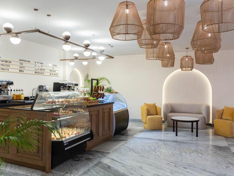 Modernes Café mit Holztheke, Vitrinen, gelben Sesseln, großem weißen Marmorboden und hängenden Lampen.