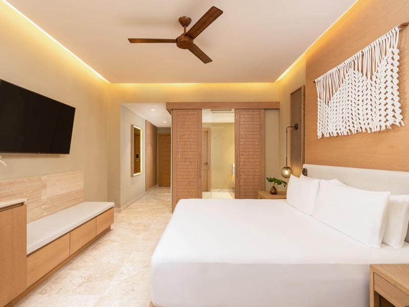 Modernes Schlafzimmer mit weißem Bett, Holzdekor, Deckenventilator und Wand-TV.