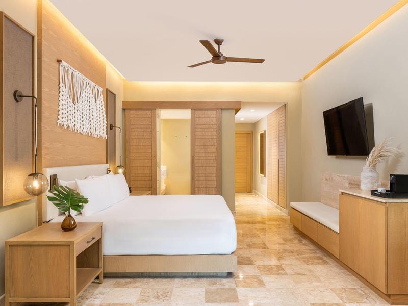 Moderner Hotelzimmer mit Doppelbett, Holzmöbeln, Fliesenboden und indirekter LED-Beleuchtung.