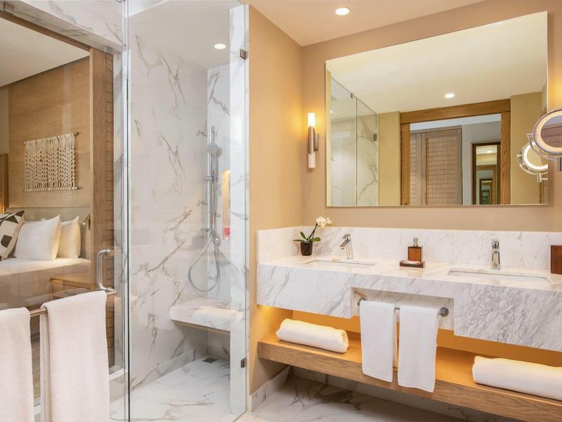 Helles Badezimmer mit Marmor, großer Spiegel, Glasdusche und weißem Handtuchständer aus Holz.