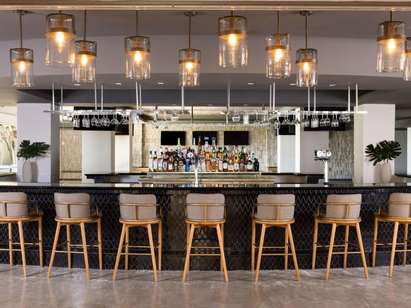 Moderner Bartresen mit schwarzen Sitzhockern, hängenden Glühlampen und Spiegelwand im Hintergrund.