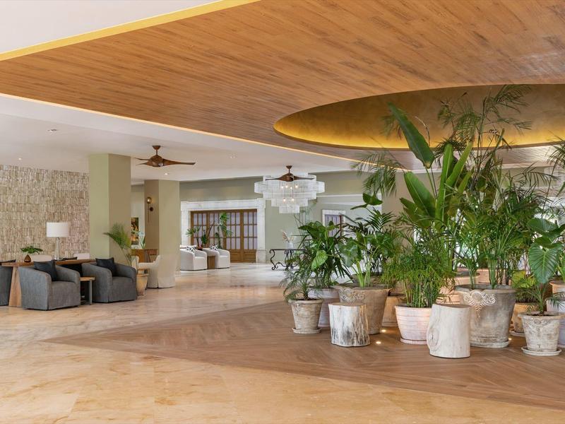 Großer Empfangsbereich mit Pflanzenarrangement, Holzdecke und steinfarbenem Boden in hellen Tönen.