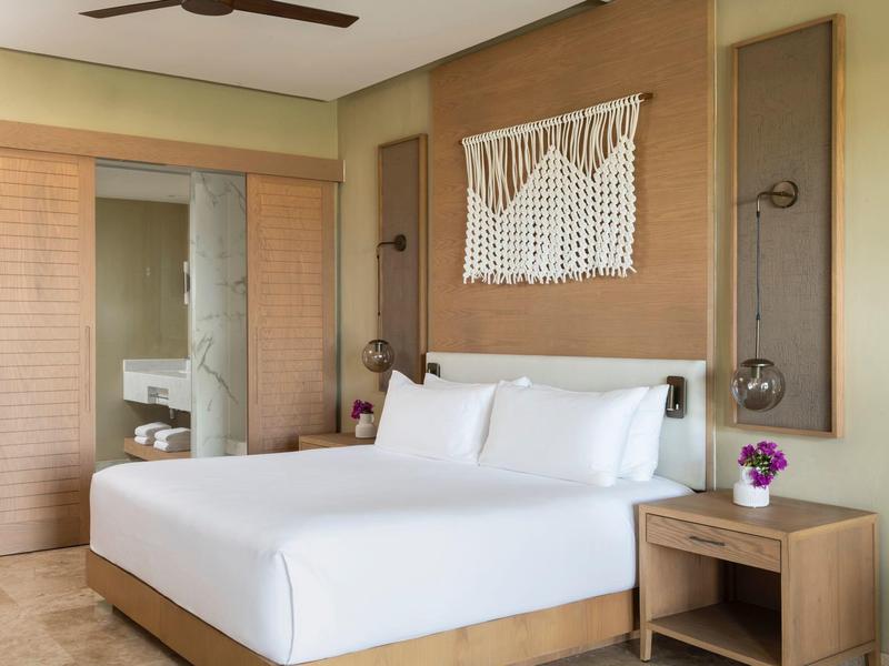 Modernes Schlafzimmer mit großem Bett, weißen Bettlaken, Holzmöbeln und dekorativer Wandgestaltung.