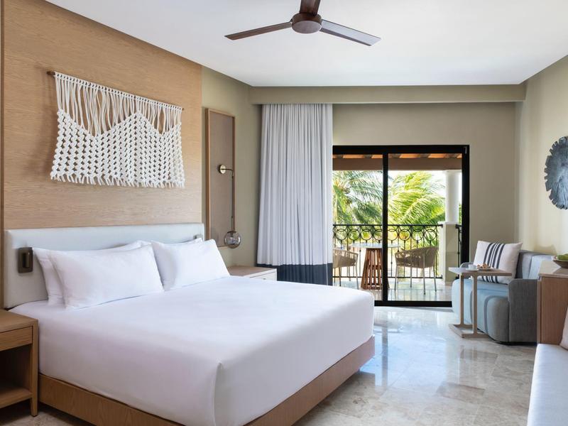 Modernes Schlafzimmer mit großem Bett, Holzrahmen, Deckenventilator und Balkon mit Pflanzenblick.