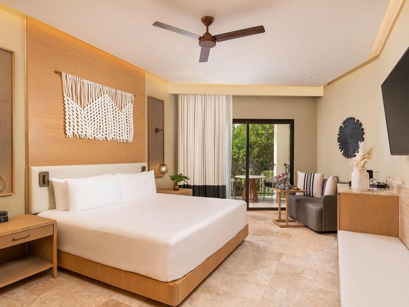 Modernes Hotelzimmer mit großem Bett, Deckenventilator, Balkon und minimalistischer Einrichtung.