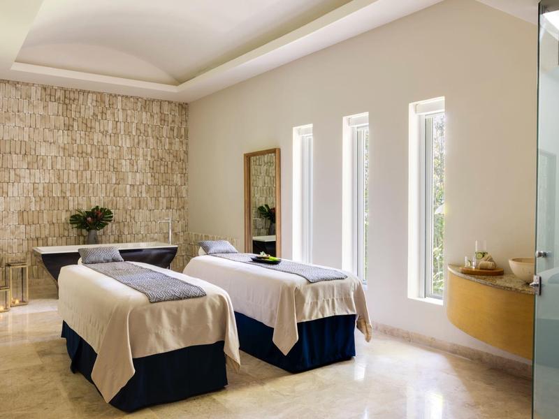 Hell eingerichteter Ruheraum mit zwei Massageliegen, drei schmalen Fenstern und Steinwand.