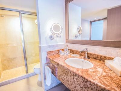 Baño de hotel luminoso con lavabo de mármol, espejo grande y ducha con puerta corrediza de vidrio.