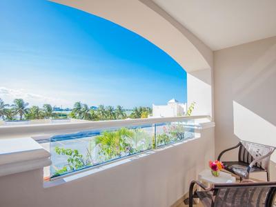 Balcón con sillas y vista a la piscina, palmeras y cielo azul a la luz del sol.