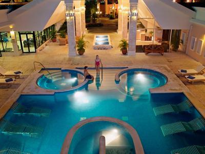 Beleuchteter Poolbereich mit Whirlpool, Liegestühlen und moderner Architektur bei Nacht.