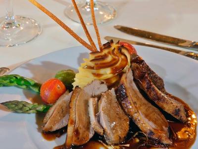 Eleganter Teller mit gebratenem Fleisch, gemüse, Sauce und knusprigen Stäbchen auf weißem Tischtuch.