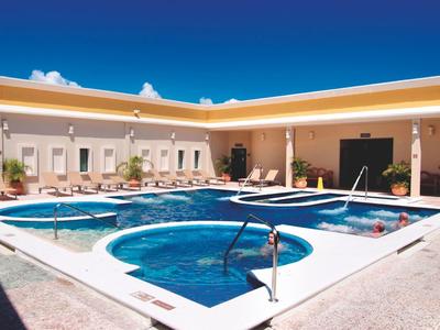 Hellblauer Pool mit runden und rechteckigen Becken, umgeben von weißen Wänden und Sonnenschirmen.