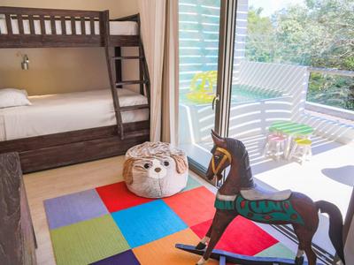 Kinderzimmer mit Etagenbett, buntem Teppich, Schaukelpferd und Balkon mit Stühlen und Pflanzen.