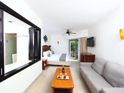 Habitación de hotel luminosa con sofá, mesa, cama y balcón con vistas a zonas verdes.