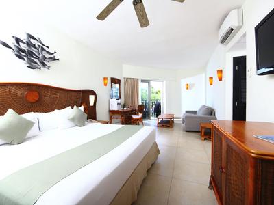 Habitación de hotel luminosa con cama doble, ventilador de techo y TV en la pared.