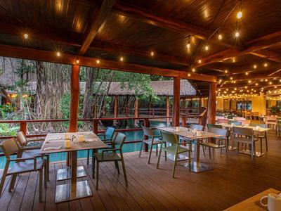 Überdachte Hotelterrasse mit Tischen, Stühlen und warmen Lichterketten, umgeben von Natur.
