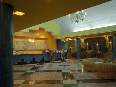 Großer, heller Hotel-Lobbybereich mit Marmorfußboden, Sitzmöbeln und Rezeption im Hintergrund.