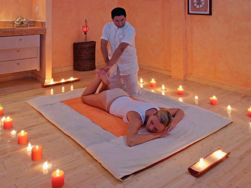 Persona riceve un massaggio ai piedi in una stanza spa accogliente illuminata da candele con pavimento in legno.