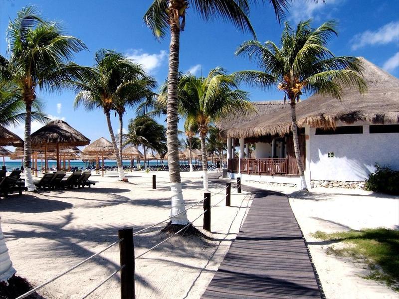 Passerella in legno con palme, sabbia e ombrelloni in un resort tropicale sulla spiaggia in una giornata soleggiata