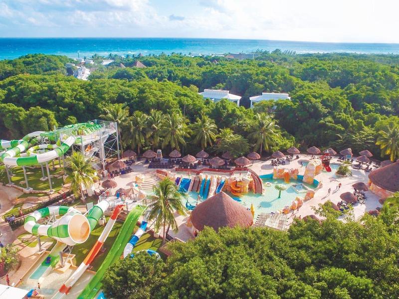 Vista di un parco acquatico con scivoli e piscine, circondato da vegetazione e mare sullo sfondo.