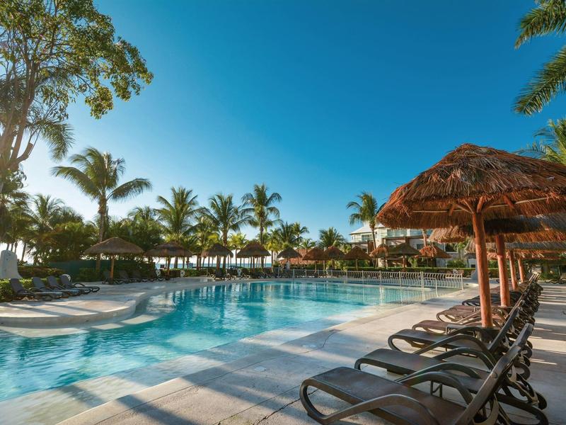 Grande piscina con lettini e palme sotto un cielo azzurro limpido.