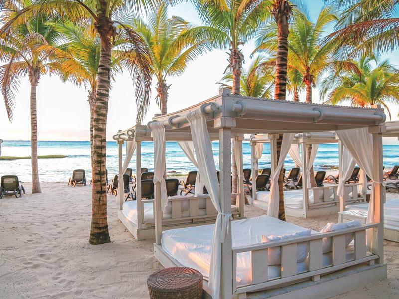 Spiaggia con letti bianchi sotto palme e vista sul mare con cielo limpido.