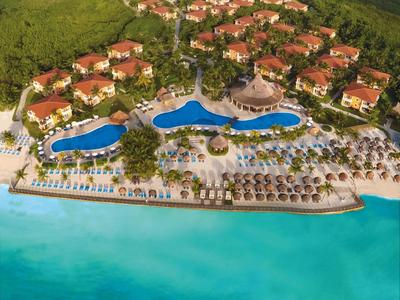 Luxusresort mit roten Dächern, großen Pools und Sandstrand an türkisfarbenem Meer.
