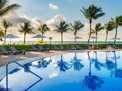 Blue pool with sun loungers and palm trees under blue sky at hotel beach.