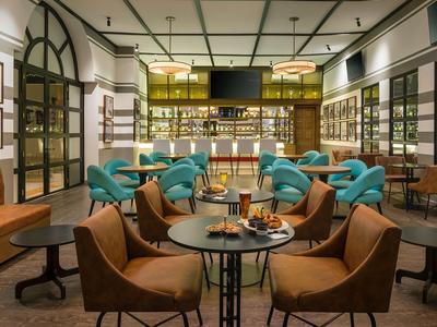 Modern lounge area with round tables, blue armchairs, and leather seats under warm lighting.