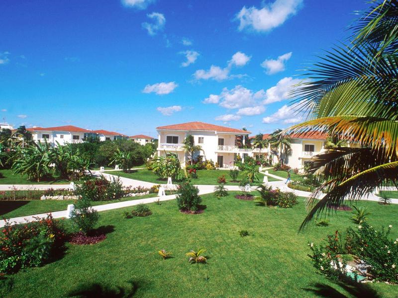 Resort con prati verdi, palme e più edifici bianchi con tetti rossi sotto un cielo blu.