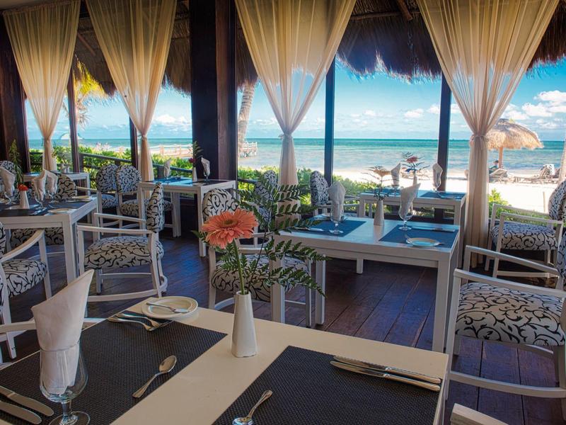 Elegante sala da pranzo fronte mare con tavoli apparecchiati e vista sull'oceano.