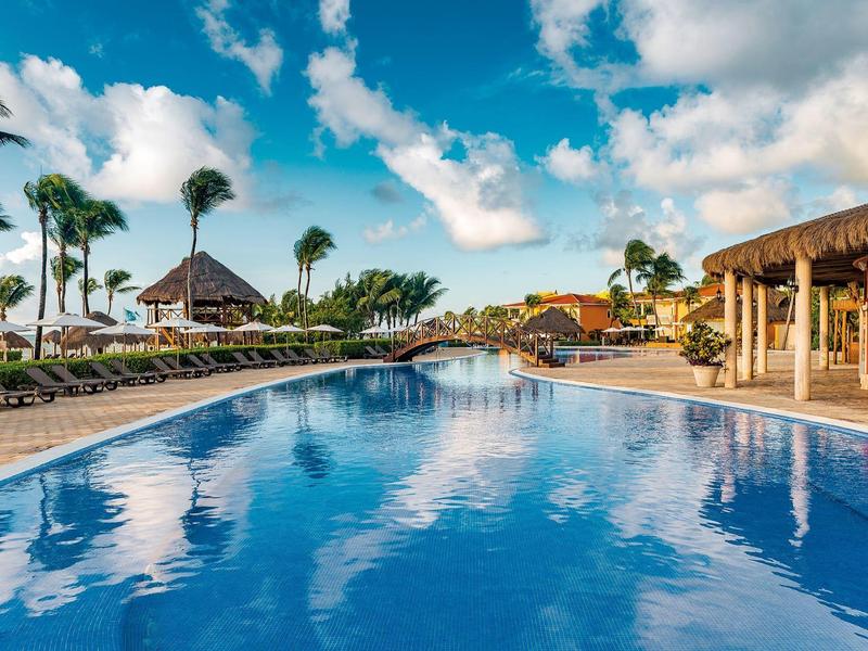 Piscina all'aperto con lettini e palme sotto un cielo parzialmente nuvoloso in un resort.