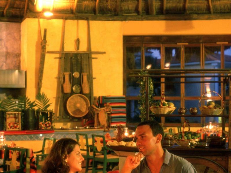 Coppia che gode di una cena a lume di candela in una stanza con tetto di paglia e decorazioni tropicali.