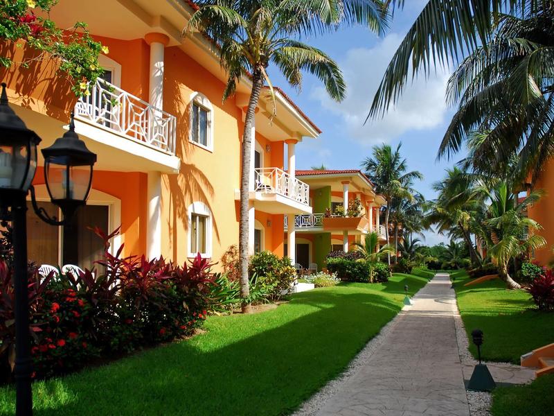 Viale tra edifici di un hotel tropicale con palme e vegetazione rigogliosa.