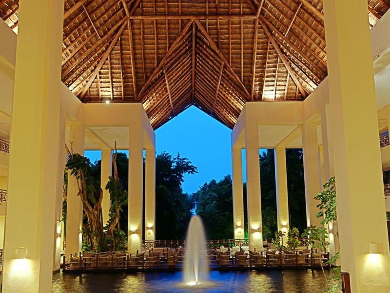 Cortile illuminato con vasca d'acqua e fontana sotto un alto tetto di legno al crepuscolo.