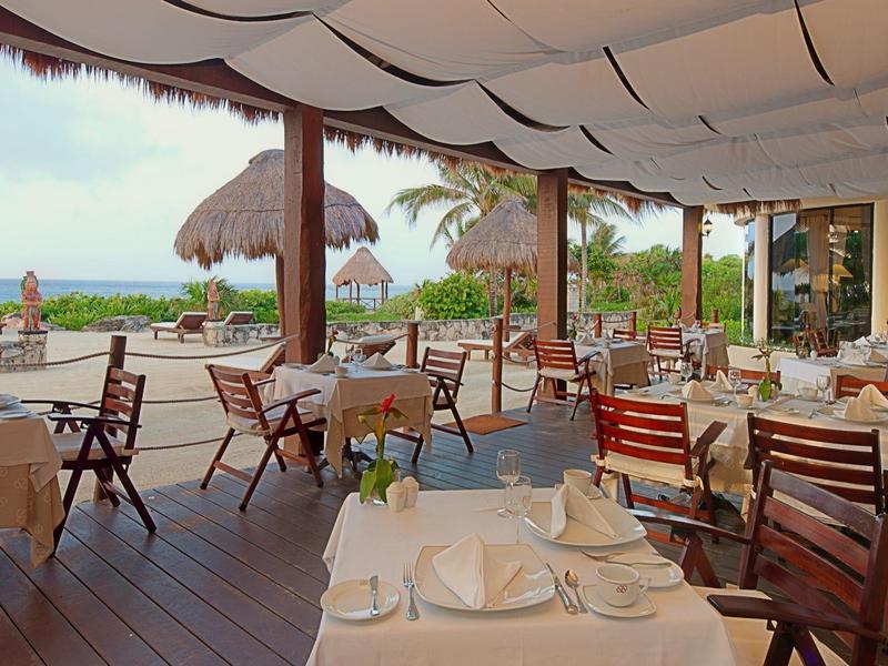Terrazza del ristorante con tavoli apparecchiati con vista su ambiente tropicale e mare.