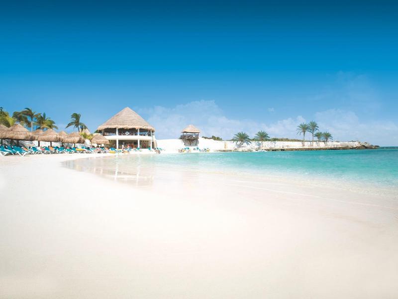 Spiaggia di sabbia bianca con acqua turchese limpida e capanni sulla spiaggia sotto un cielo azzurro.