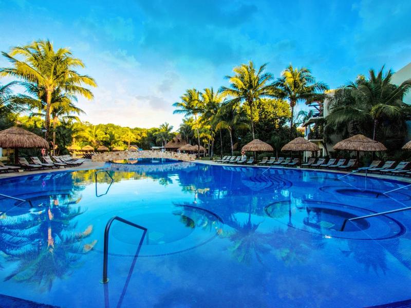 Grande piscina con lettini e palme sotto un cielo azzurro in un resort.