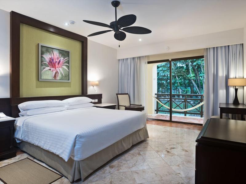 Stanza d'albergo moderna con letto grande, ventilatore a soffitto e balcone con vista sul verde.